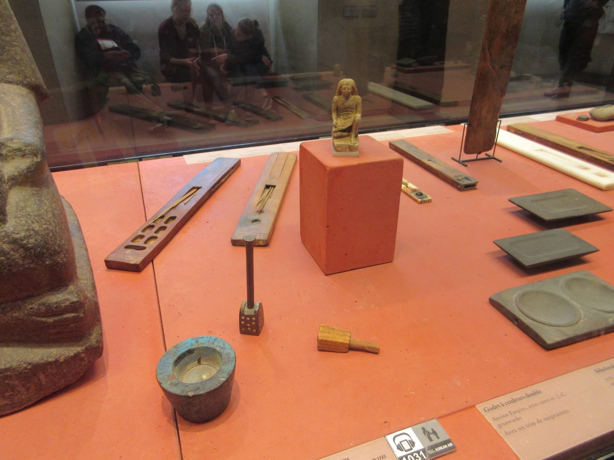 A third sculpture of a scribe, surrounded by examples of scribal tools.